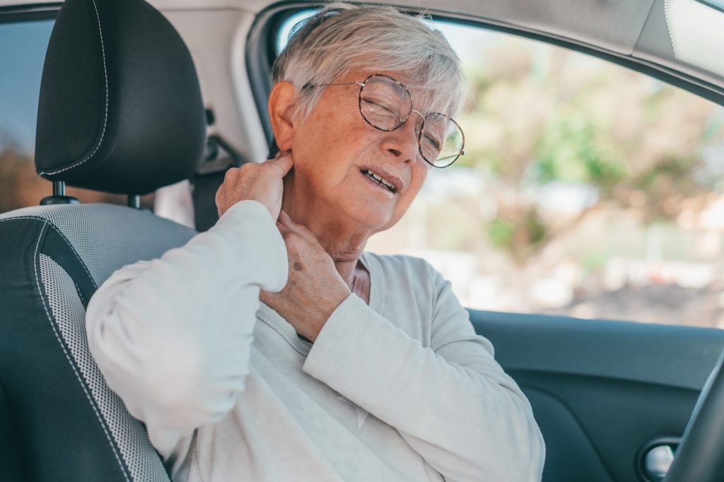 Rear view of old woman having neck pain while driving a car. One senior or mature people feeling bad